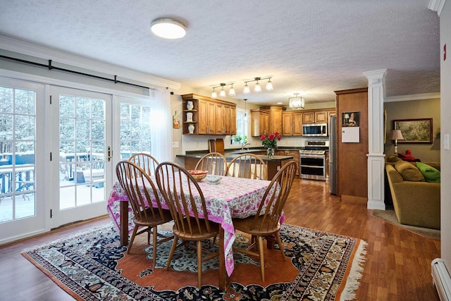 dining space featuring a baseboard heating unit, ornamental molding, a textured ceiling, dark hardwood / wood-style flooring, and decorative columns