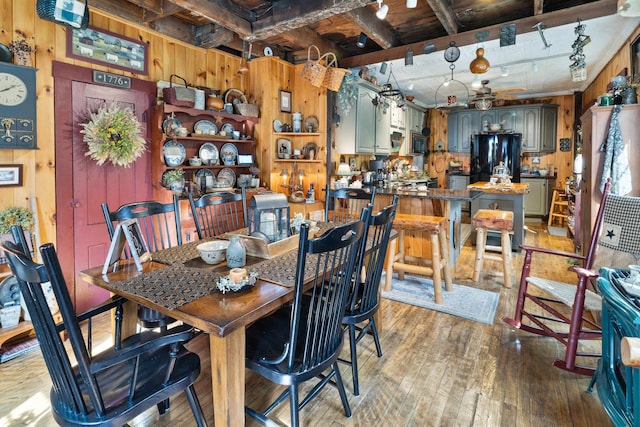 dining room with beam ceiling, ceiling fan, wood walls, track lighting, and hardwood / wood-style flooring