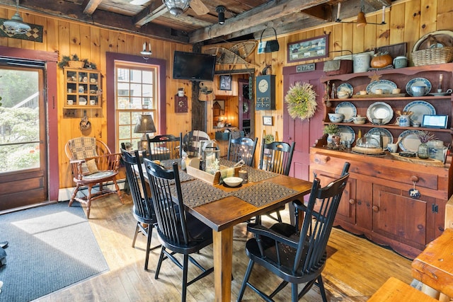 dining space with wooden ceiling, baseboard heating, beamed ceiling, wood walls, and light wood-type flooring