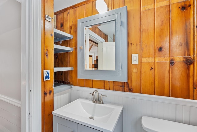 bathroom with wood walls, vanity, and toilet