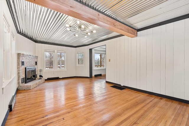 unfurnished living room with a brick fireplace, beam ceiling, light wood-type flooring, and an inviting chandelier