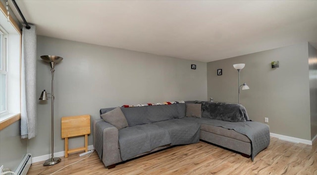 living room with a baseboard heating unit, light wood-type flooring, and a healthy amount of sunlight