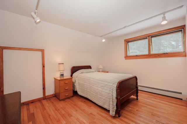 bedroom featuring lofted ceiling, rail lighting, a baseboard heating unit, and light hardwood / wood-style flooring