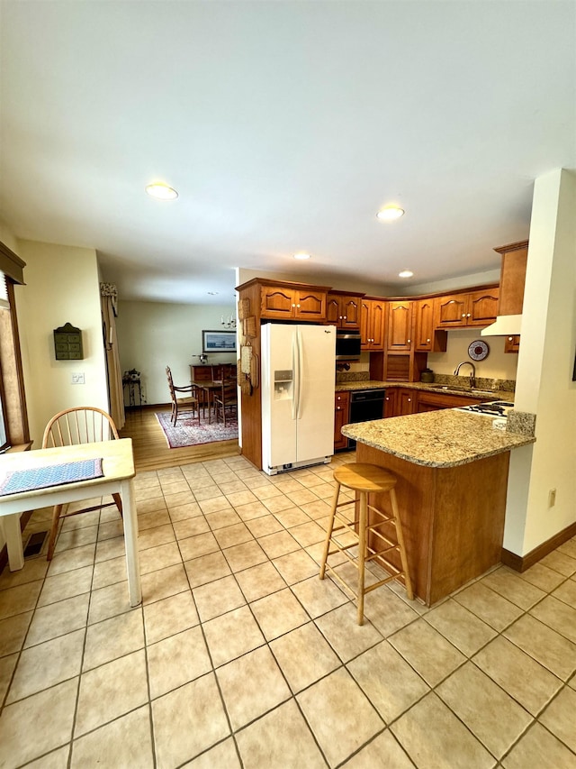 kitchen featuring white refrigerator with ice dispenser, light stone countertops, dishwasher, a kitchen breakfast bar, and sink