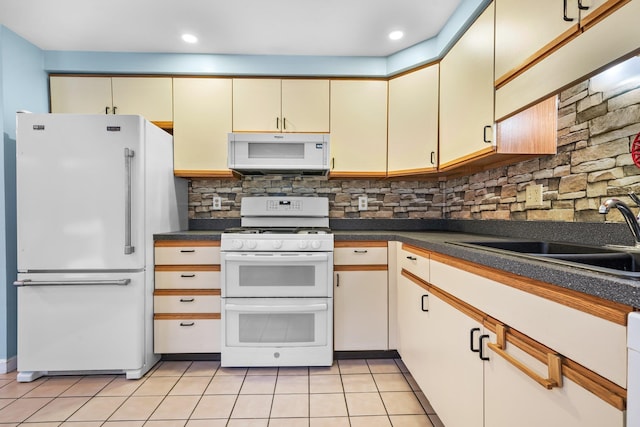 kitchen featuring white appliances, cream cabinetry, sink, and light tile patterned floors