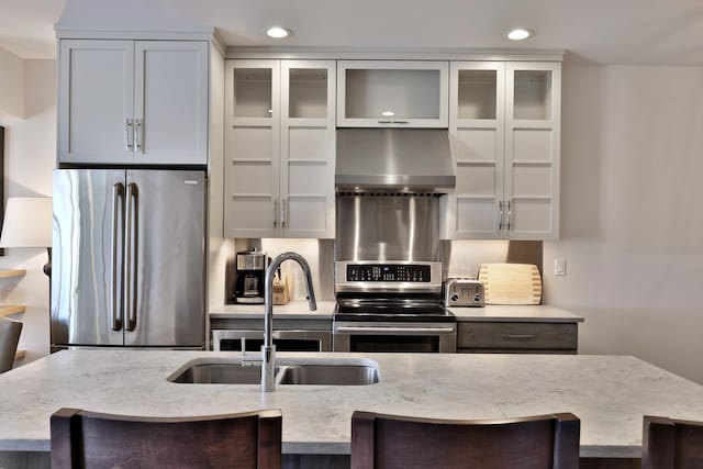 kitchen with exhaust hood, appliances with stainless steel finishes, white cabinets, light stone counters, and sink