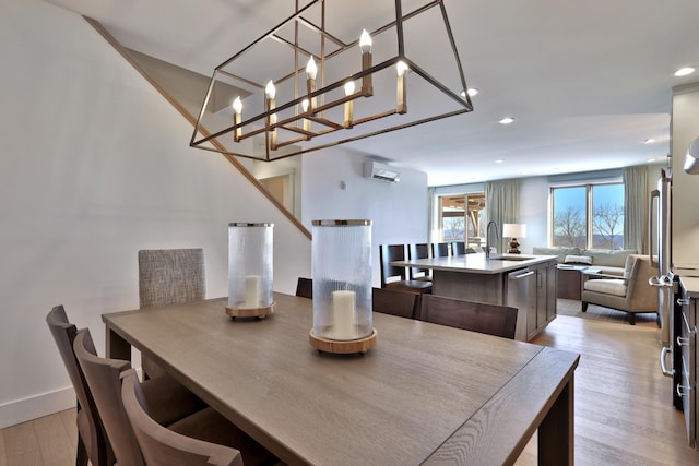 dining room featuring a wall mounted air conditioner, a notable chandelier, sink, and light hardwood / wood-style flooring