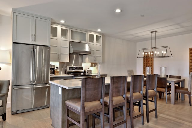 kitchen featuring a center island, light hardwood / wood-style flooring, hanging light fixtures, appliances with stainless steel finishes, and a kitchen breakfast bar