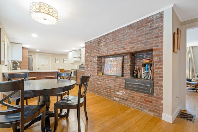 dining area with ornamental molding, light wood-type flooring, and brick wall