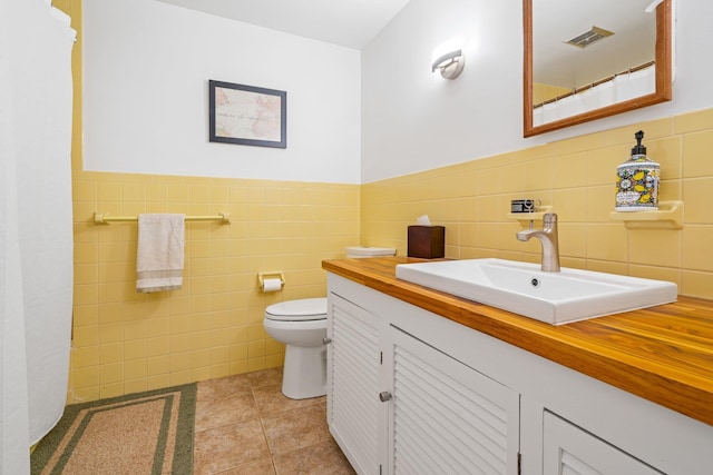 bathroom featuring toilet, tile patterned floors, vanity, and tile walls