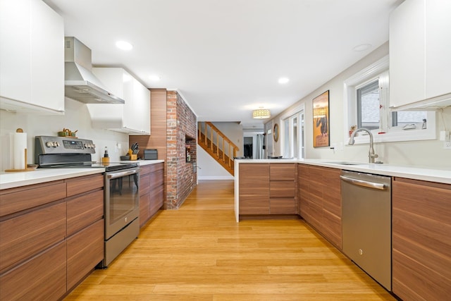 kitchen with wall chimney exhaust hood, stainless steel appliances, light hardwood / wood-style floors, white cabinets, and sink