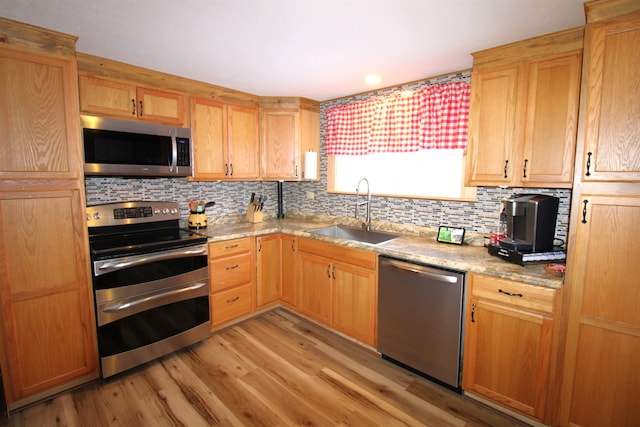 kitchen with sink, light wood-type flooring, decorative backsplash, light stone countertops, and appliances with stainless steel finishes