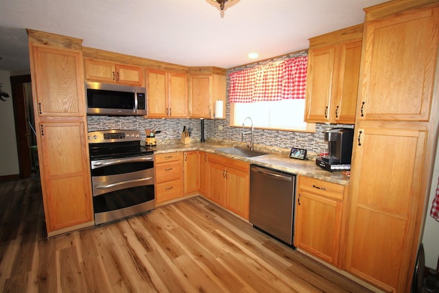 kitchen with appliances with stainless steel finishes, light wood-type flooring, decorative backsplash, and sink