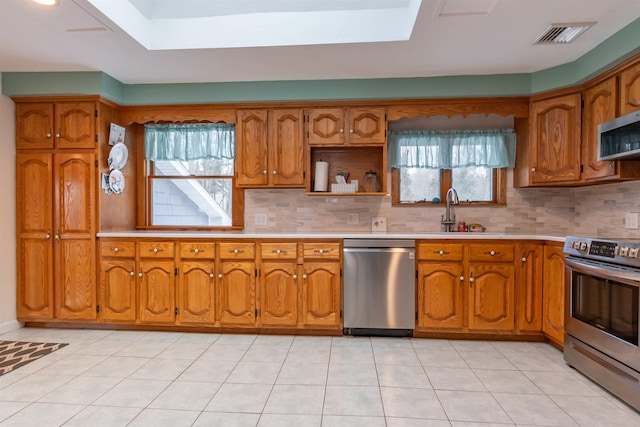 kitchen with stainless steel appliances, light tile patterned floors, a skylight, backsplash, and sink