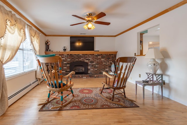 sitting room with baseboard heating, light wood-type flooring, ceiling fan, ornamental molding, and a fireplace