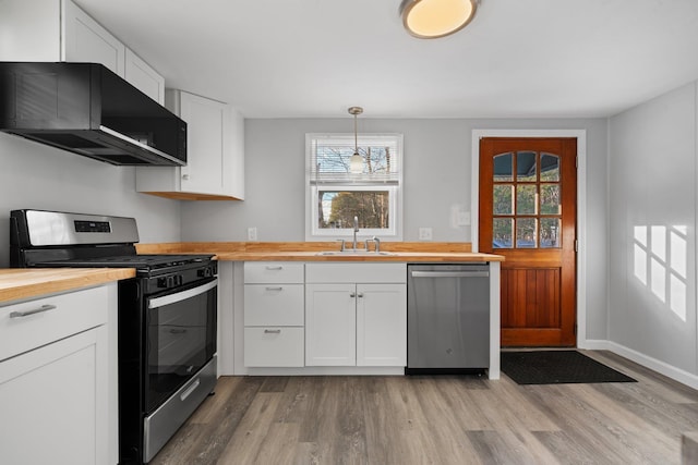 kitchen with appliances with stainless steel finishes, butcher block countertops, white cabinets, decorative light fixtures, and sink