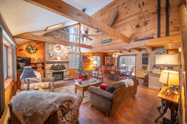 living room featuring wood walls, hardwood / wood-style floors, beam ceiling, ceiling fan, and a stone fireplace