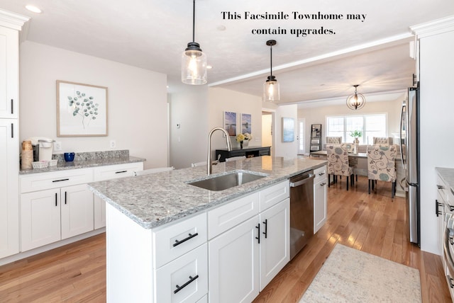 kitchen featuring white cabinets, hanging light fixtures, an island with sink, stainless steel appliances, and sink