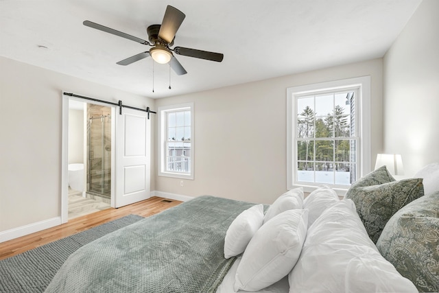 bedroom with ensuite bathroom, ceiling fan, a barn door, and light hardwood / wood-style flooring