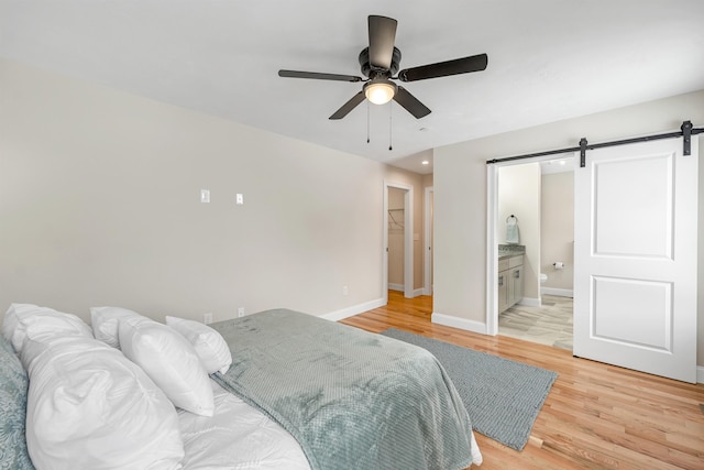 bedroom featuring a closet, a barn door, light hardwood / wood-style floors, ceiling fan, and ensuite bathroom