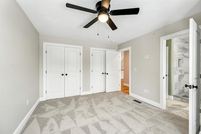 unfurnished bedroom with light colored carpet, connected bathroom, ceiling fan, and multiple closets