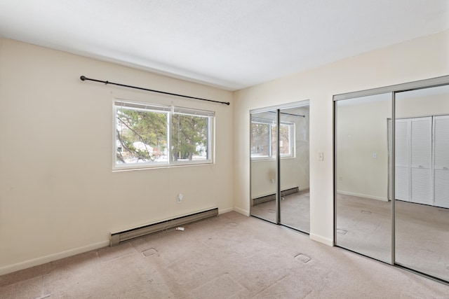 unfurnished bedroom with baseboard heating, light colored carpet, and two closets