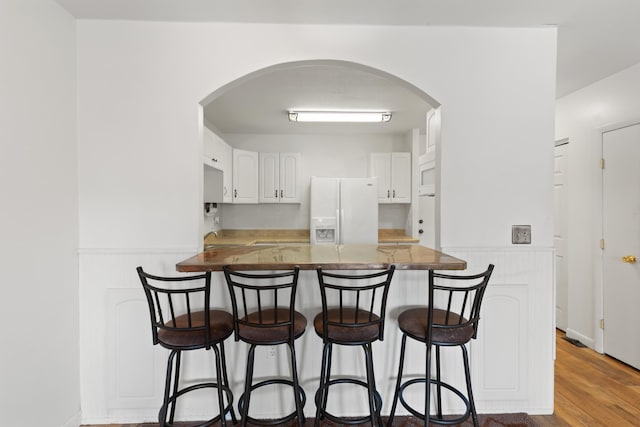 kitchen with white cabinets, a kitchen bar, light hardwood / wood-style floors, kitchen peninsula, and white fridge with ice dispenser