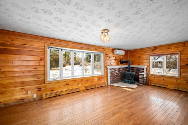 unfurnished living room featuring wood-type flooring, an AC wall unit, a healthy amount of sunlight, and a wood stove