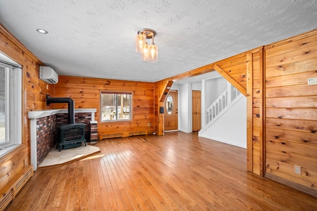 unfurnished living room with baseboard heating, a wall mounted AC, wood walls, and a wood stove