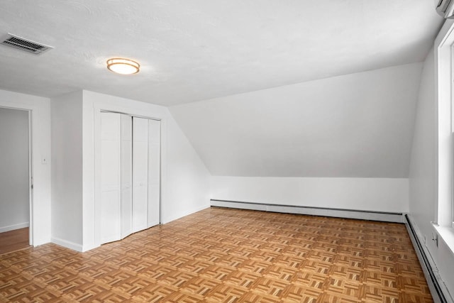 additional living space featuring light parquet flooring, vaulted ceiling, and a baseboard heating unit