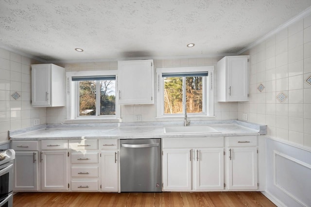 kitchen featuring light wood-type flooring, ornamental molding, white cabinets, stainless steel dishwasher, and sink