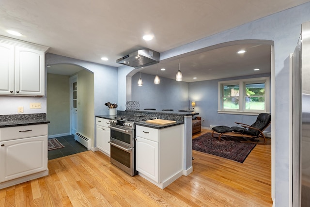 kitchen featuring range with two ovens, decorative light fixtures, wall chimney range hood, light wood-type flooring, and white cabinetry