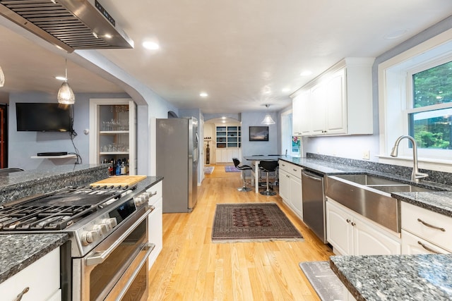 kitchen with hanging light fixtures, stainless steel appliances, white cabinets, dark stone countertops, and sink