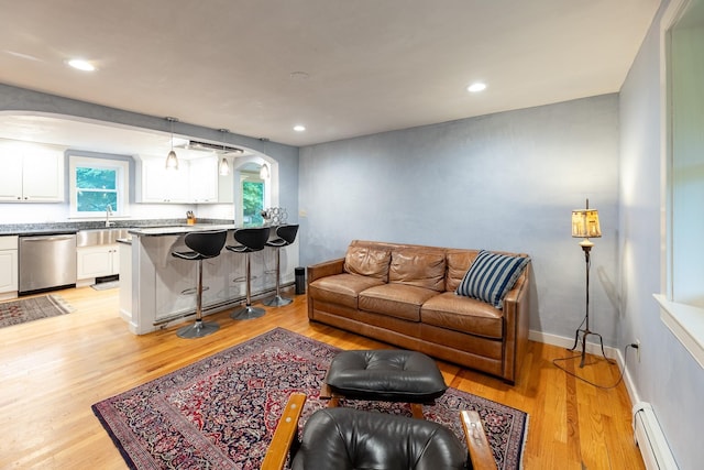 living room featuring sink, baseboard heating, and light hardwood / wood-style flooring