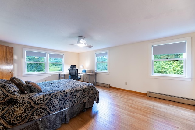 bedroom with ceiling fan, baseboard heating, light wood-type flooring, and multiple windows