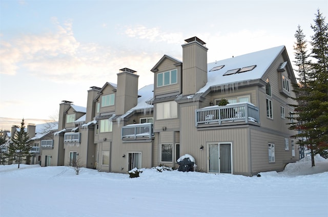 69 Daybreak Dr Unit H-102, Ludlow, VT 05149 - snow covered rear of property featuring an AC wall unit, a chimney, and a balcony