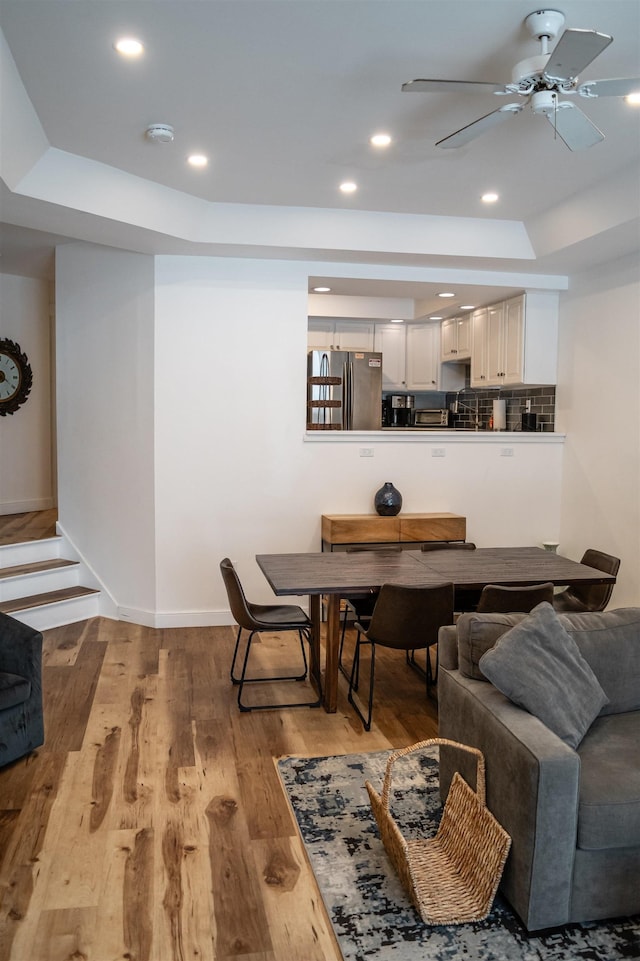 dining room with a raised ceiling, ceiling fan, and light hardwood / wood-style floors