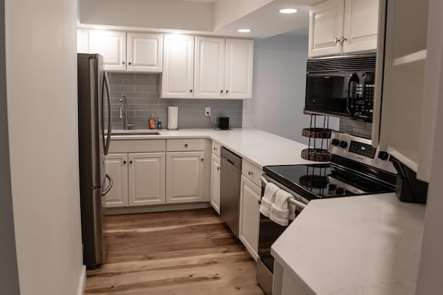 kitchen with stainless steel appliances, sink, white cabinets, light hardwood / wood-style floors, and tasteful backsplash