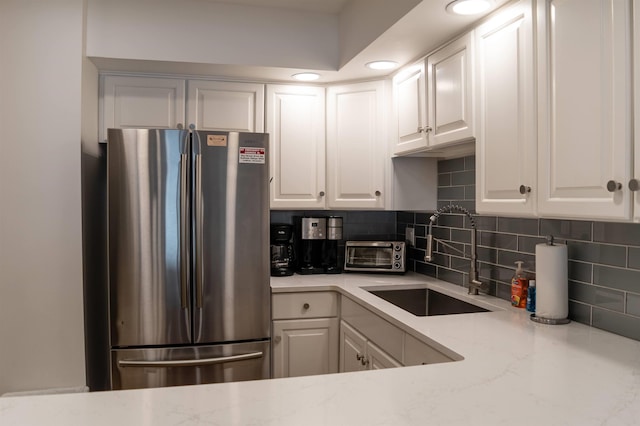 kitchen featuring white cabinets, stainless steel fridge, light stone counters, and sink