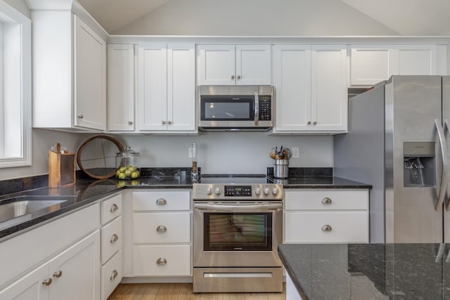 kitchen featuring lofted ceiling, white cabinets, dark stone countertops, and appliances with stainless steel finishes