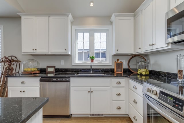 kitchen with stainless steel appliances, dark stone countertops, white cabinets, and sink