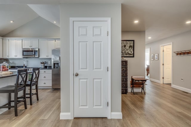 kitchen featuring white cabinets, light wood-type flooring, vaulted ceiling, and stainless steel appliances