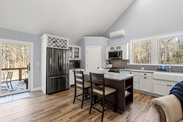 kitchen with appliances with stainless steel finishes, a wall mounted AC, a center island, white cabinets, and backsplash