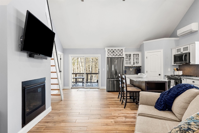 living room with a wall mounted AC, light wood-type flooring, and vaulted ceiling