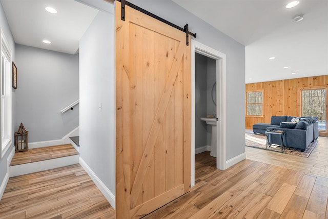 hallway with a barn door, light hardwood / wood-style floors, and wooden walls