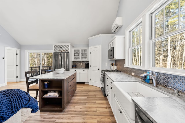 kitchen with appliances with stainless steel finishes, a kitchen island, white cabinetry, lofted ceiling, and tasteful backsplash