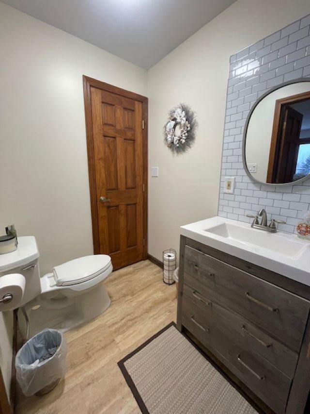 bathroom featuring toilet, wood-type flooring, vanity, and decorative backsplash