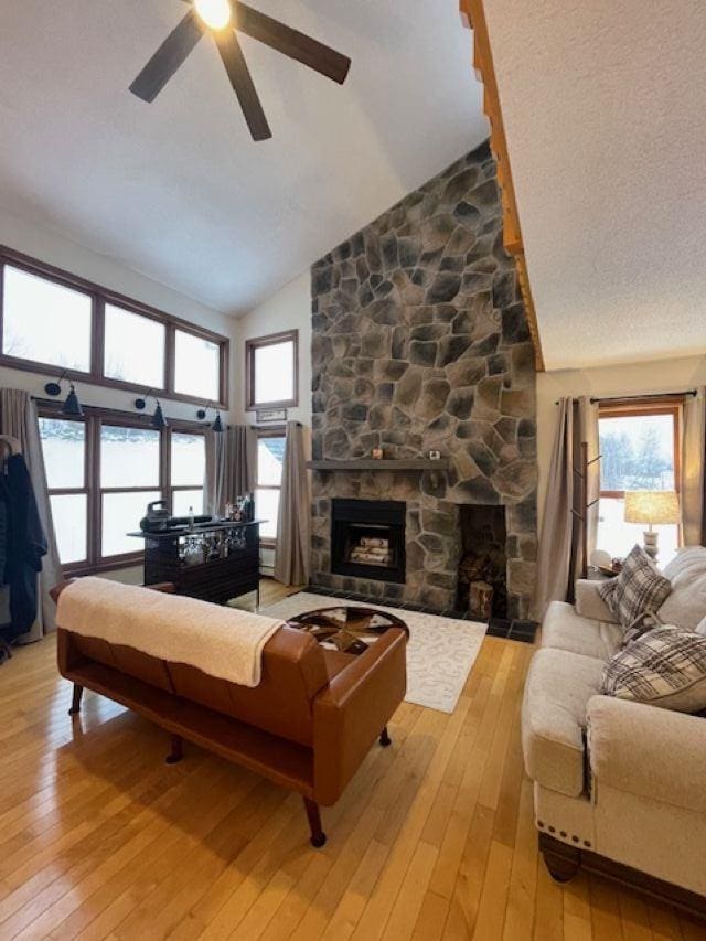 living room with hardwood / wood-style floors, high vaulted ceiling, ceiling fan, and a stone fireplace