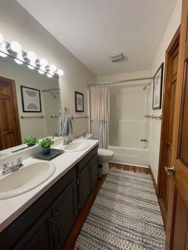 full bathroom with shower / tub combo, hardwood / wood-style floors, toilet, vanity, and a textured ceiling