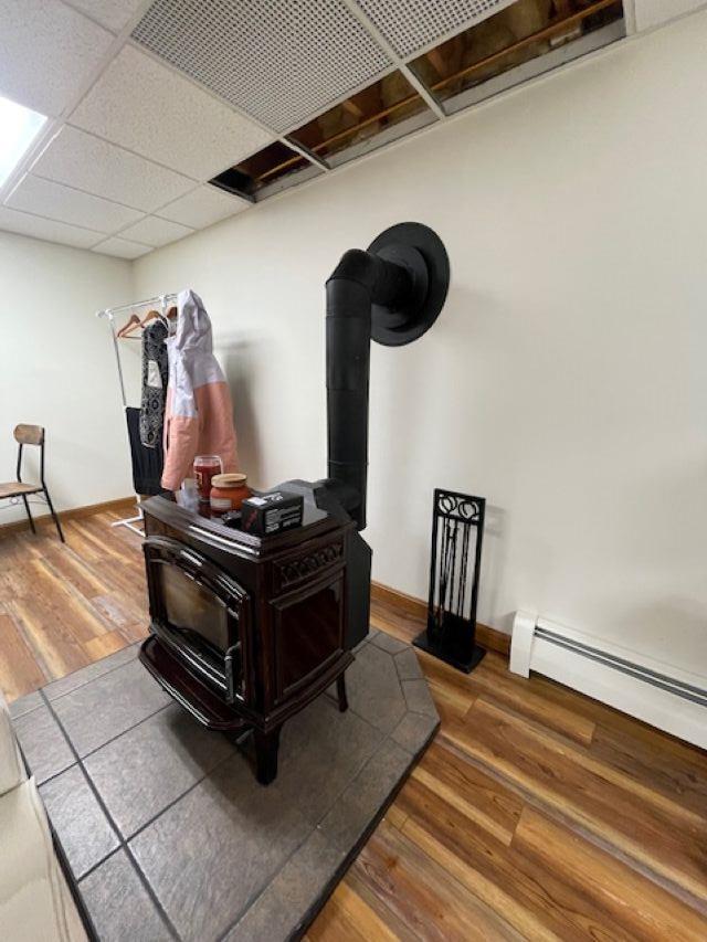 room details featuring wood-type flooring, baseboard heating, a drop ceiling, and a wood stove